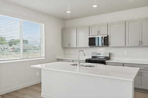 *DISCLAIMER*  Interior package and colors may vary. Kitchen featuring gray cabinetry, stainless steel appliances, light wood-style flooring, a center island with sink, and recessed lighting