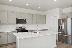 *DISCLAIMER*  Interior package and colors may vary. Kitchen with gray cabinets, stainless steel appliances, a center island with sink, light wood-style floors, and light stone countertops