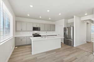 *DISCLAIMER*  Interior package and colors may vary. Kitchen with gray cabinets, stainless steel appliances, a center island with sink, light wood-style floors, and recessed lighting