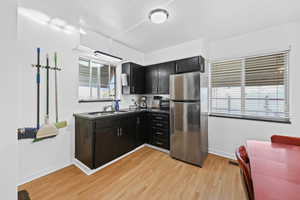 Kitchen featuring freestanding refrigerator, dark cabinetry, dark countertops, and light wood-style floors