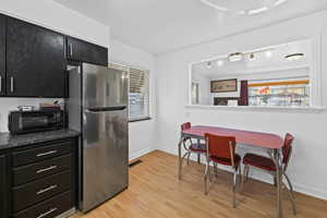 Kitchen with dark cabinets, freestanding refrigerator, light wood-type flooring, and dark stone counters