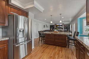 Kitchen with stainless steel fridge with ice dispenser, ornamental molding, a kitchen bar, a textured ceiling, and light wood-type flooring