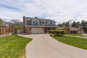 Traditional-style home featuring a chimney, covered porch, brick siding, an attached garage, and driveway
