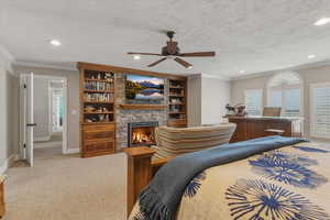 Carpeted bedroom featuring a textured ceiling, recessed lighting, a stone fireplace, ceiling fan, and crown molding