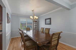 Dining space with light wood finished floors, crown molding, a chandelier, and a textured ceiling