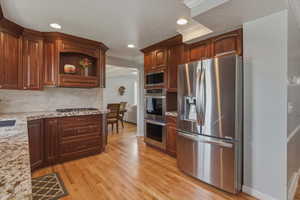 Kitchen featuring stainless steel appliances, light stone counters, light wood finished floors, ornamental molding, and recessed lighting