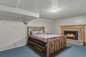 Carpeted bedroom featuring a textured ceiling and a brick fireplace