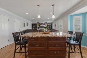 Kitchen with a breakfast bar area, a center island, ornamental molding, hanging light fixtures, and open floor plan