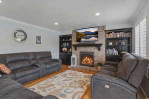 Living room with crown molding, a brick fireplace, wood finished floors, built in shelves, and recessed lighting