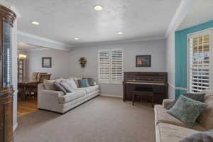 Living area featuring ornamental molding, a textured ceiling, carpet flooring, and suspended lighting