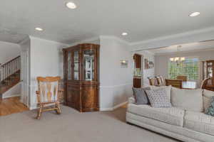 Living room with suspended lighting, ornamental molding, and light carpet