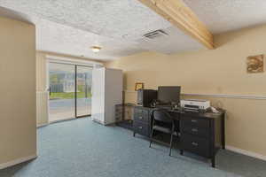 Home office with light colored carpet, a textured ceiling, and beam ceiling