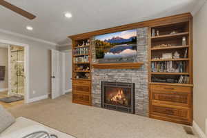 Living area with light carpet, ornamental molding, a stone fireplace, a textured ceiling, and a ceiling fan