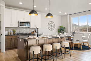 Two tone kitchen featuring light wood-style floors, backsplash, dual tone cabinets, hanging light fixtures, and stainless steel appliances