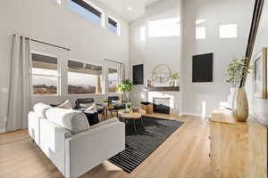 Living area featuring plenty of natural light, a glass covered fireplace, light wood-style flooring, and a high ceiling