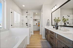 Bathroom featuring a walk in closet, double vanity, a stall shower, a bath, and light wood-style floors