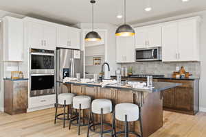 Kitchen featuring tasteful backsplash, stainless steel appliances, decorative light fixtures, dual tone cabinetry, and light wood finished floors