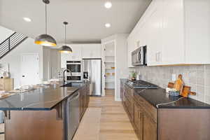 Kitchen featuring stainless steel appliances, an island with sink, light wood-style flooring, hanging light fixtures, and a breakfast bar area