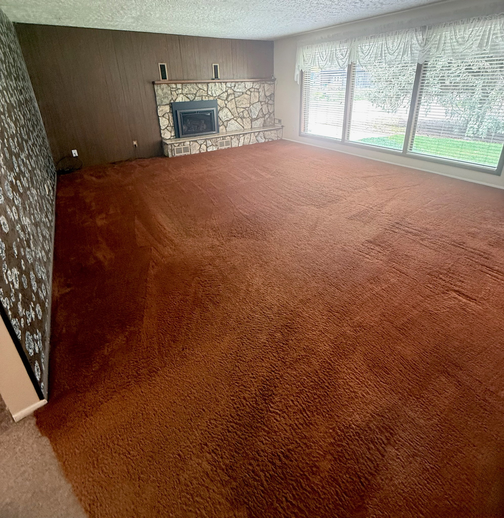 Unfurnished living room featuring carpet floors, wooden walls, a stone fireplace, and a textured ceiling
