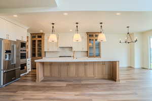 Kitchen with glass fronted cabinets, stainless steel appliances, a large island, two tone color scheme, and light wood-type flooring