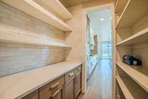 Bar area featuring open shelves, light wood-type flooring, light stone counters, wood finish cabinets, and a chandelier