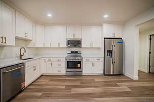 Kitchen featuring white cabinetry, stainless steel appliances, light wood finished floors, recessed lighting, and light stone counters