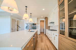 Kitchen featuring light wood-style flooring, two tone color scheme, stainless steel appliances, a large island, and pendant lighting