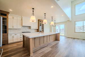 Two tone kitchen with glass fronted cabinets, two tone cabinets, hanging light fixtures, backsplash, and a spacious island