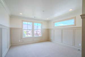Empty room featuring a decorative wall, wainscoting, light carpet, recessed lighting, and crown molding