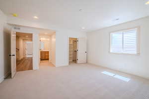 Unfurnished bedroom with a spacious closet, recessed lighting, light carpet, and ensuite bath