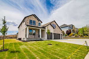 View of front of house with board and batten siding, a porch, stone siding, a front yard, and driveway