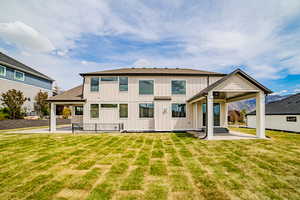 Back of property featuring board and batten siding, a patio area, a lawn, and a shingled roof