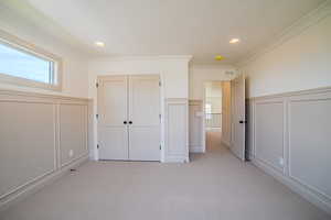 Unfurnished bedroom with a decorative wall, wainscoting, light carpet, a closet, and crown molding