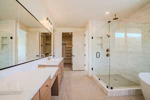Full bath with a stall shower, a spacious closet, double vanity, light tile patterned floors, and a freestanding tub