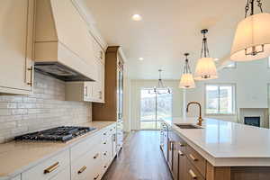 Two tone kitchen featuring dual tone cabinetry, light stone counters, a kitchen island with sink, light wood-style flooring, and stainless steel gas stovetop