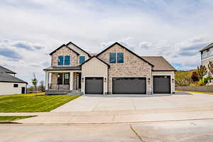 View of front facade with board and batten siding, stone siding, a porch, a front lawn, and driveway