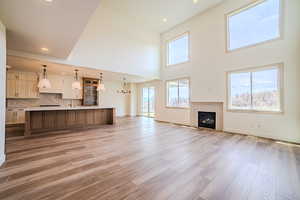 Unfurnished living room with hanging lights, light wood-type flooring, a fireplace, and a high ceiling