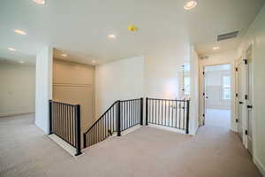 Hallway with light colored carpet, an upstairs landing, and recessed lighting
