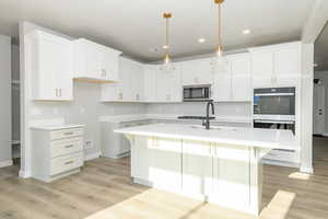 Kitchen with a kitchen island with sink, white cabinetry, a breakfast bar area, light wood-style floors, and stainless steel appliances