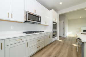 Kitchen with light wood-type flooring, recessed lighting, stainless steel appliances, white cabinetry, and light stone countertops