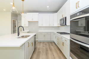 Kitchen featuring stainless steel appliances, light wood-type flooring, a center island with sink, light stone counters, and pendant lighting