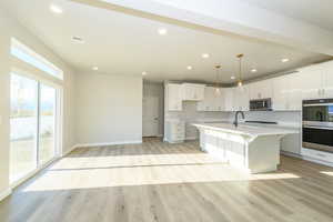 Kitchen featuring a kitchen bar, light wood finished floors, a center island with sink, and white cabinets