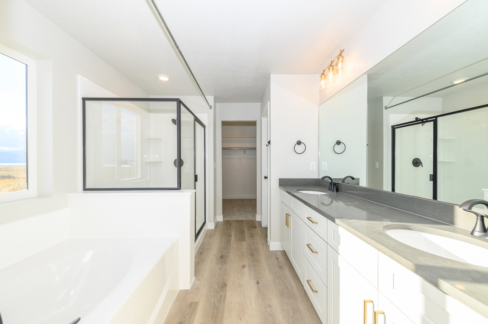 Full bath with double vanity, a stall shower, a garden tub, a walk in closet, and light wood-style floors
