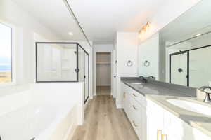 Full bath with double vanity, a stall shower, a garden tub, a walk in closet, and light wood-style floors