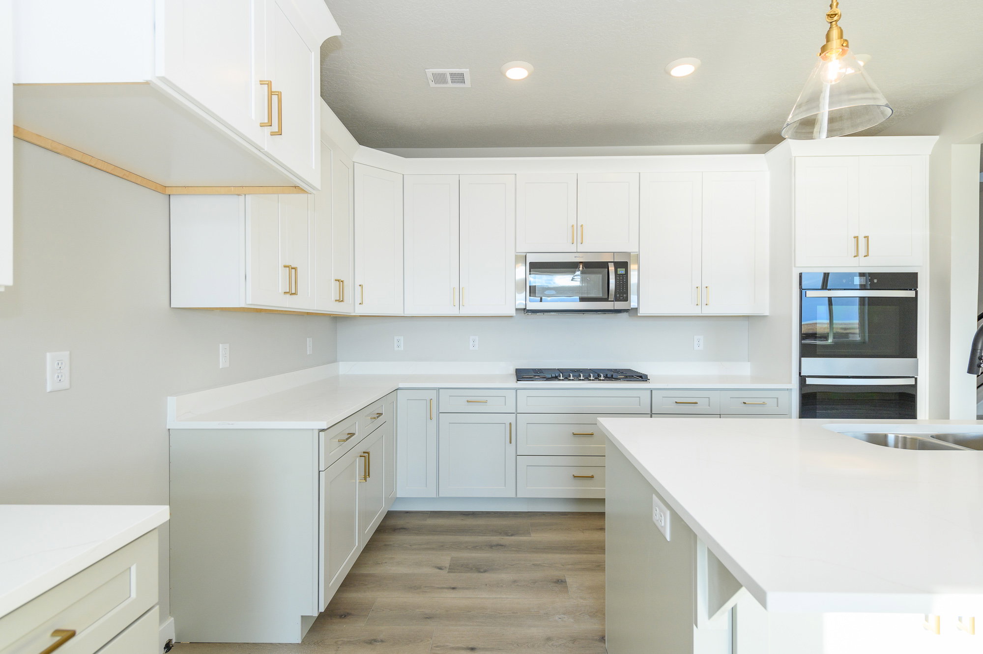 Kitchen featuring white cabinetry, light wood finished floors, stainless steel appliances, light stone counters, and hanging light fixtures