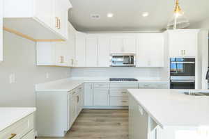 Kitchen featuring white cabinetry, light wood finished floors, stainless steel appliances, light stone counters, and hanging light fixtures