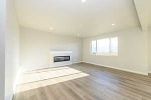Unfurnished living room featuring light wood-style floors, recessed lighting, and a glass covered fireplace
