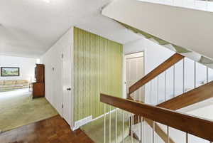 Corridor with a textured ceiling, carpet, wallpapered walls, and parquet floors