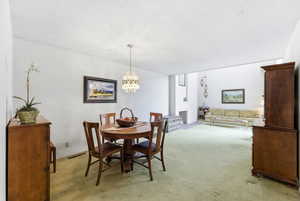 Dining room featuring a fireplace, light colored carpet, a textured ceiling, and hanging lights