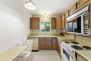 Kitchen with stainless steel appliances, wood finish cabinets, light countertops, and wallpapered walls